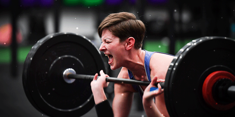 Woman lifting barbell in gym, intense expression, CrossFit strength training exercise