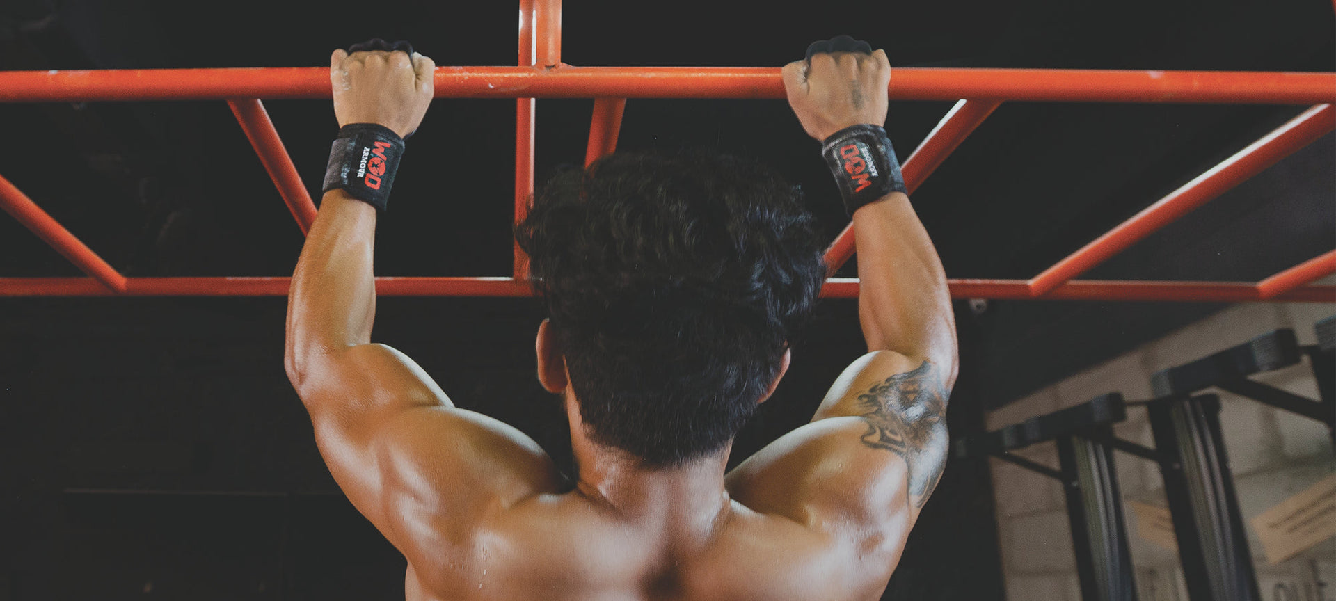 Athlete doing pull-ups on red bar, wearing wrist supports, functional fitness gym setting