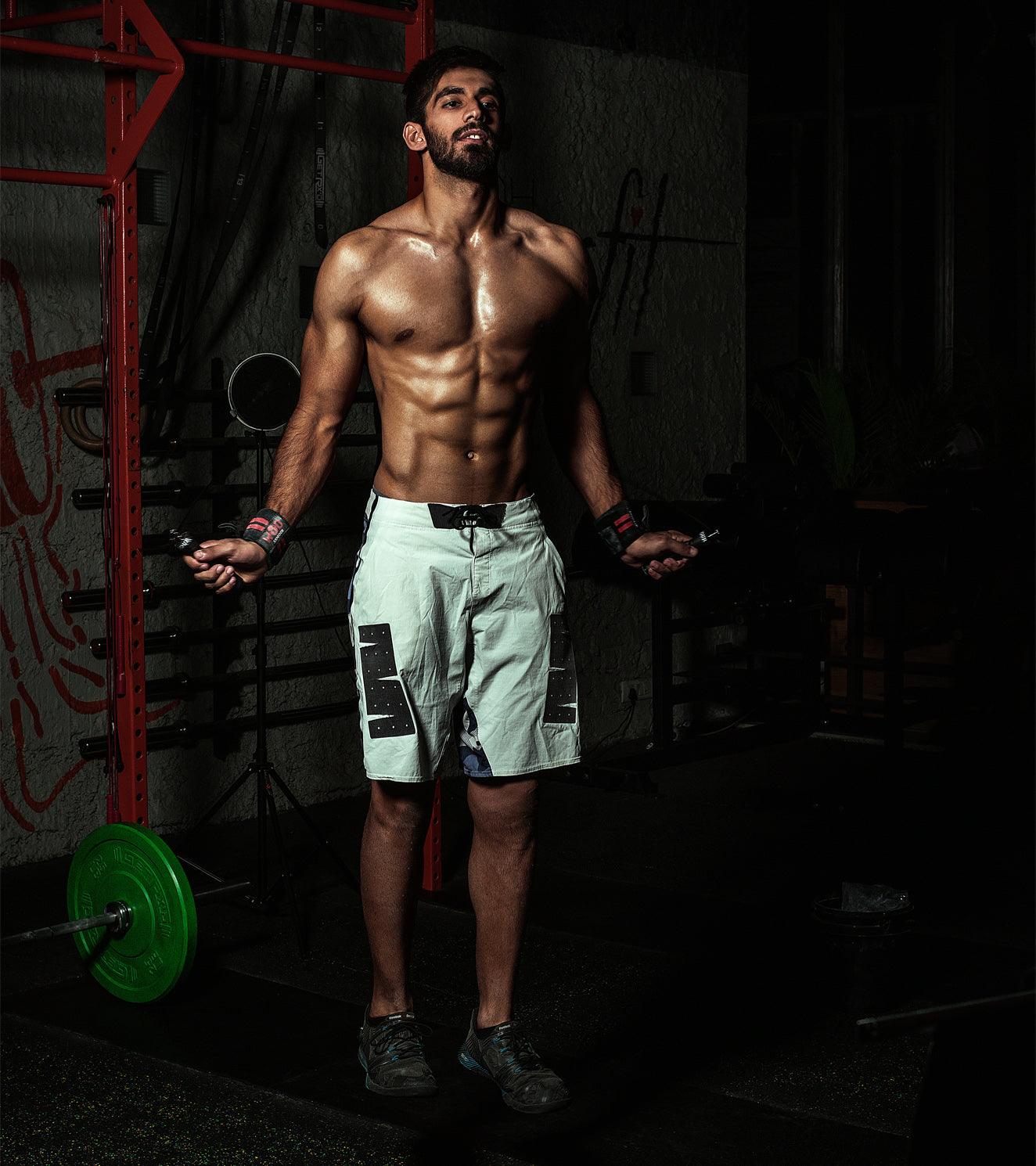 Muscular man skipping rope in gym, wearing workout shorts and wrist wraps, functional fitness