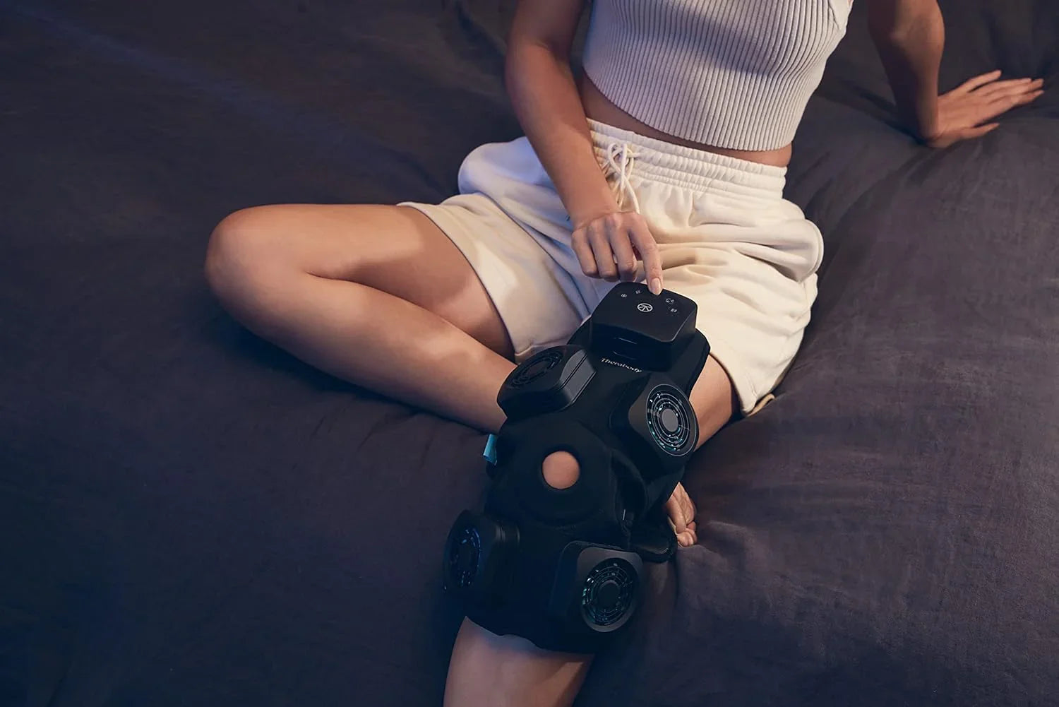 Person using an electronic knee therapy device while sitting on a bed