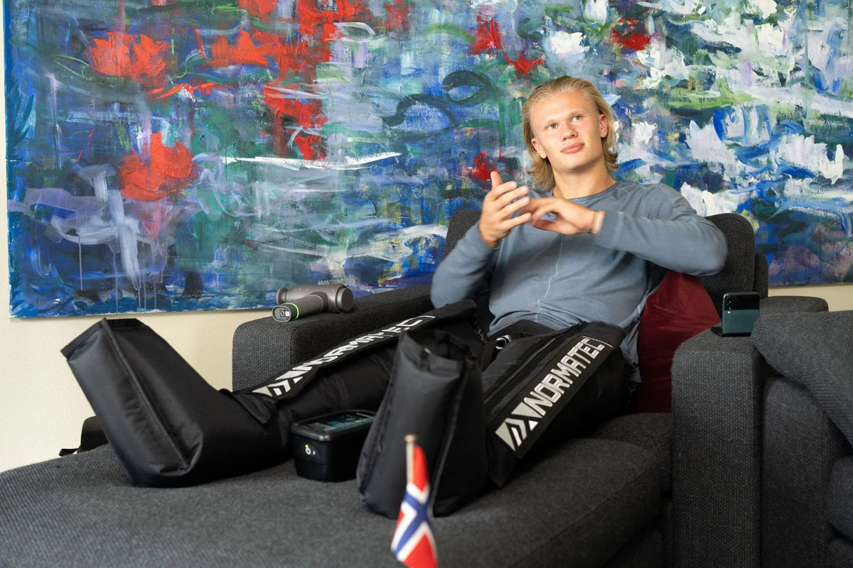 Man using NormaTec compression leg boots for recovery while sitting in a chair.