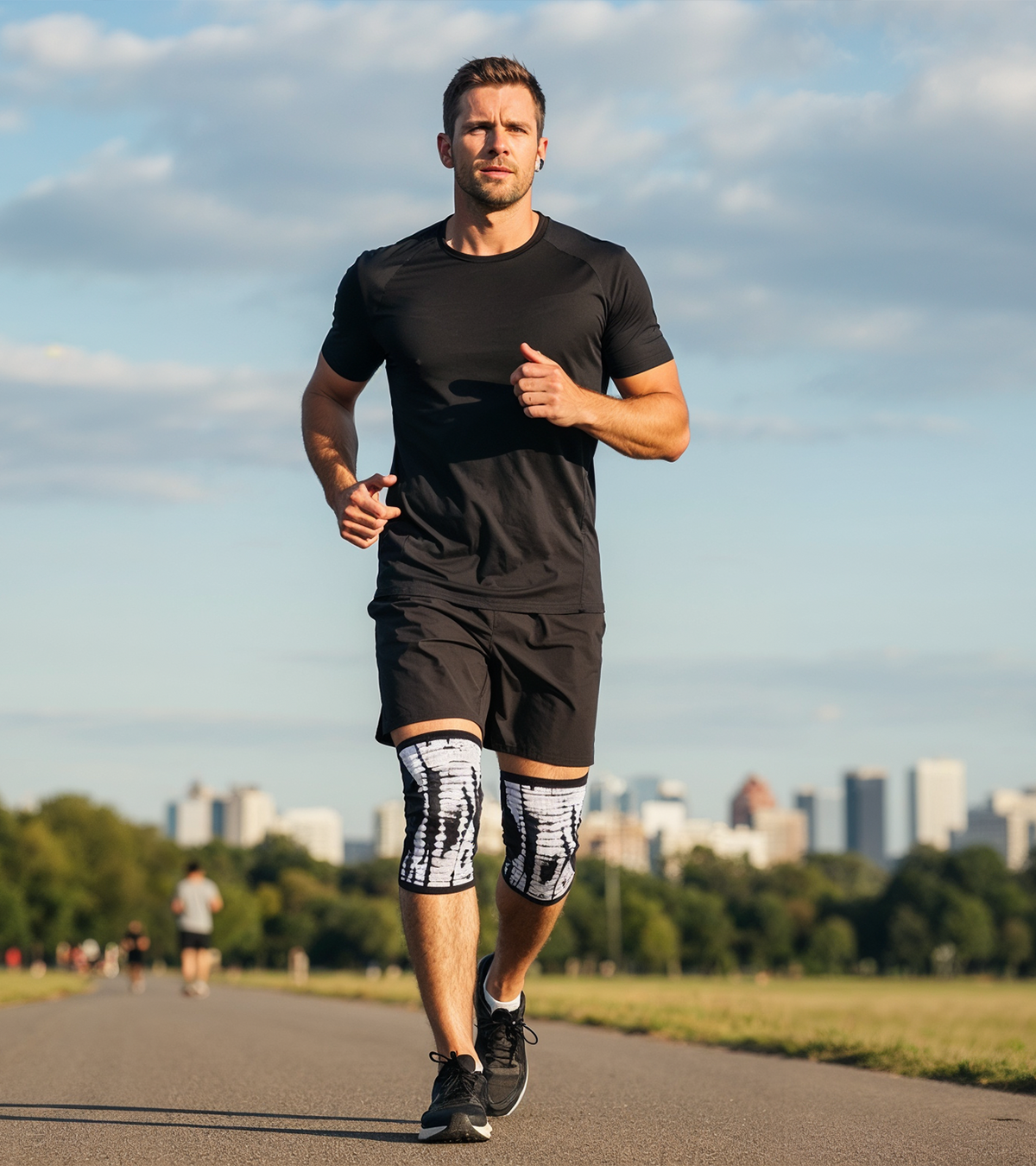 Man running outdoors wearing black athletic gear and patterned knee compression sleeves.