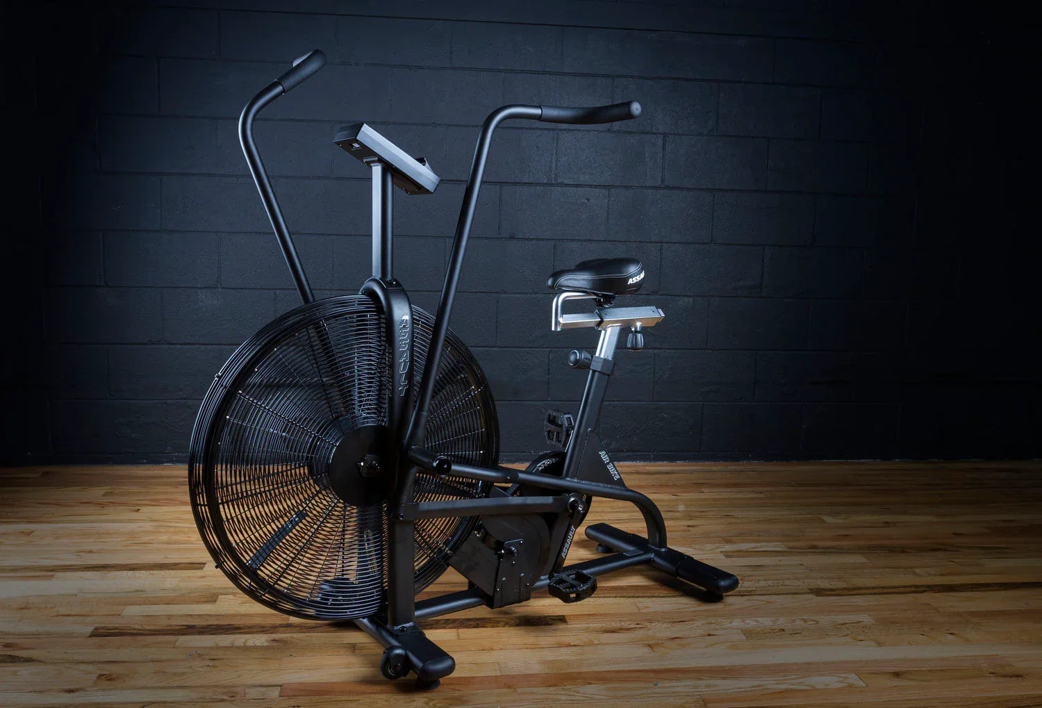Air bike fitness equipment on wooden floor against dark gym wall