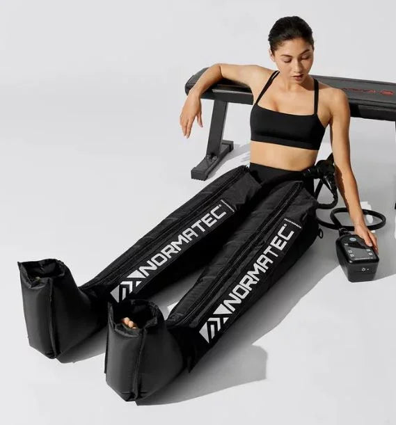 Woman using Normatec leg compression recovery boots in a fitness setting