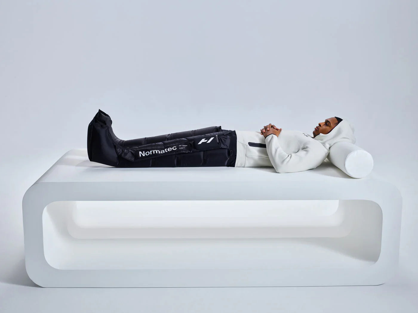 Athlete using Normatec leg recovery boots on a modern white bench, recovery therapy session