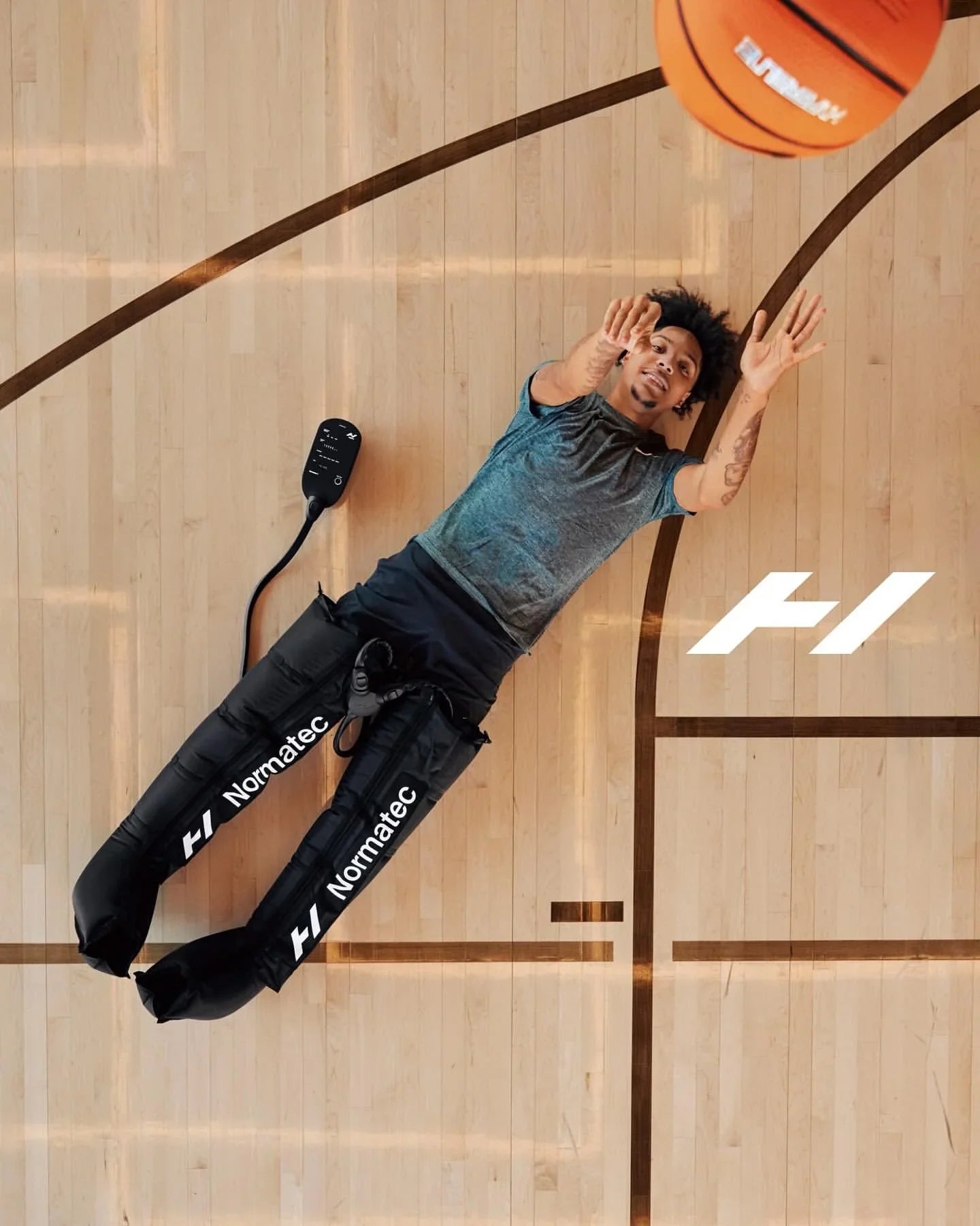 Athlete using Normatec leg recovery boots on basketball court reaching for basketball