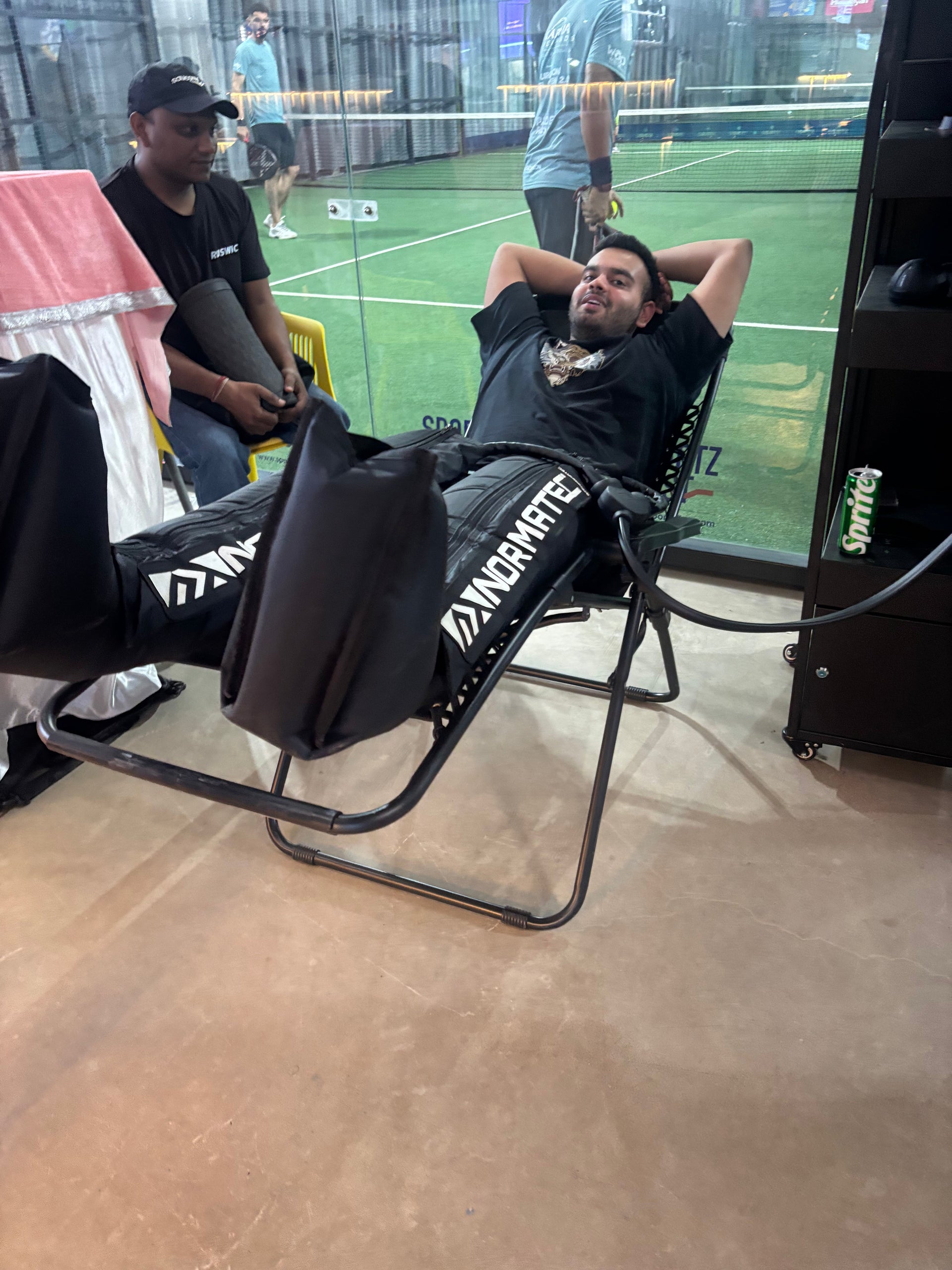 Athlete using Normatec leg recovery boots in a gym next to a sports court