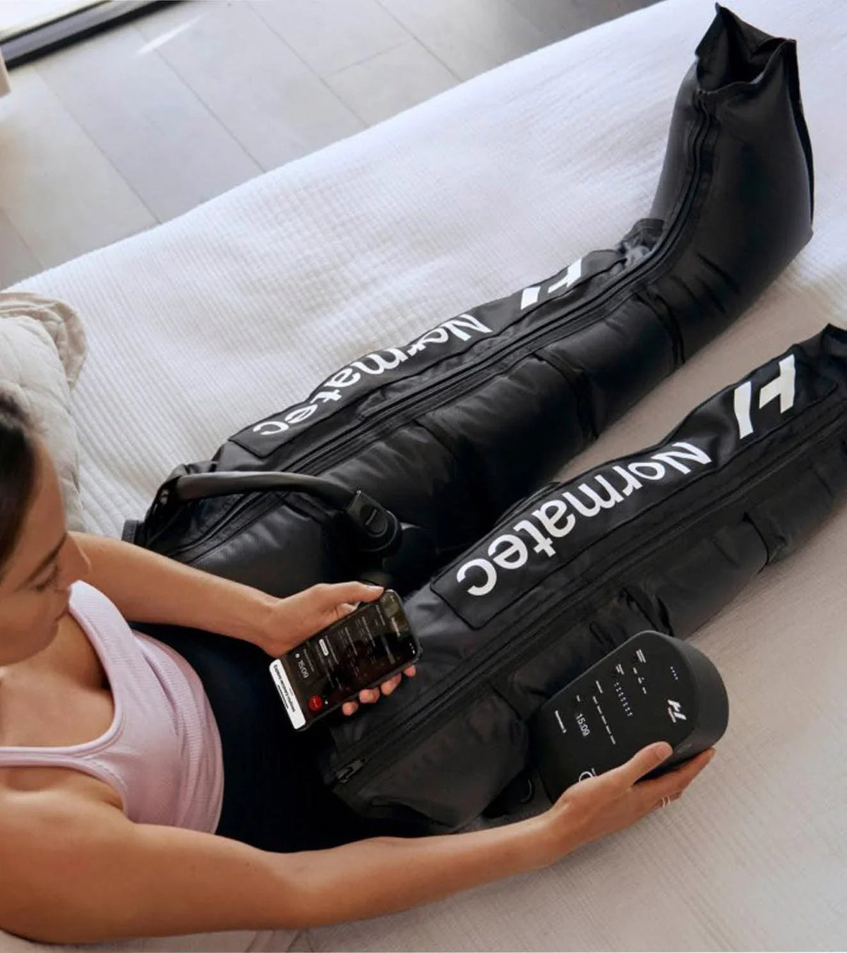 Athlete relaxing in Hyperice Normatec 3 compression boots, adjusting the control unit and Hyperice app