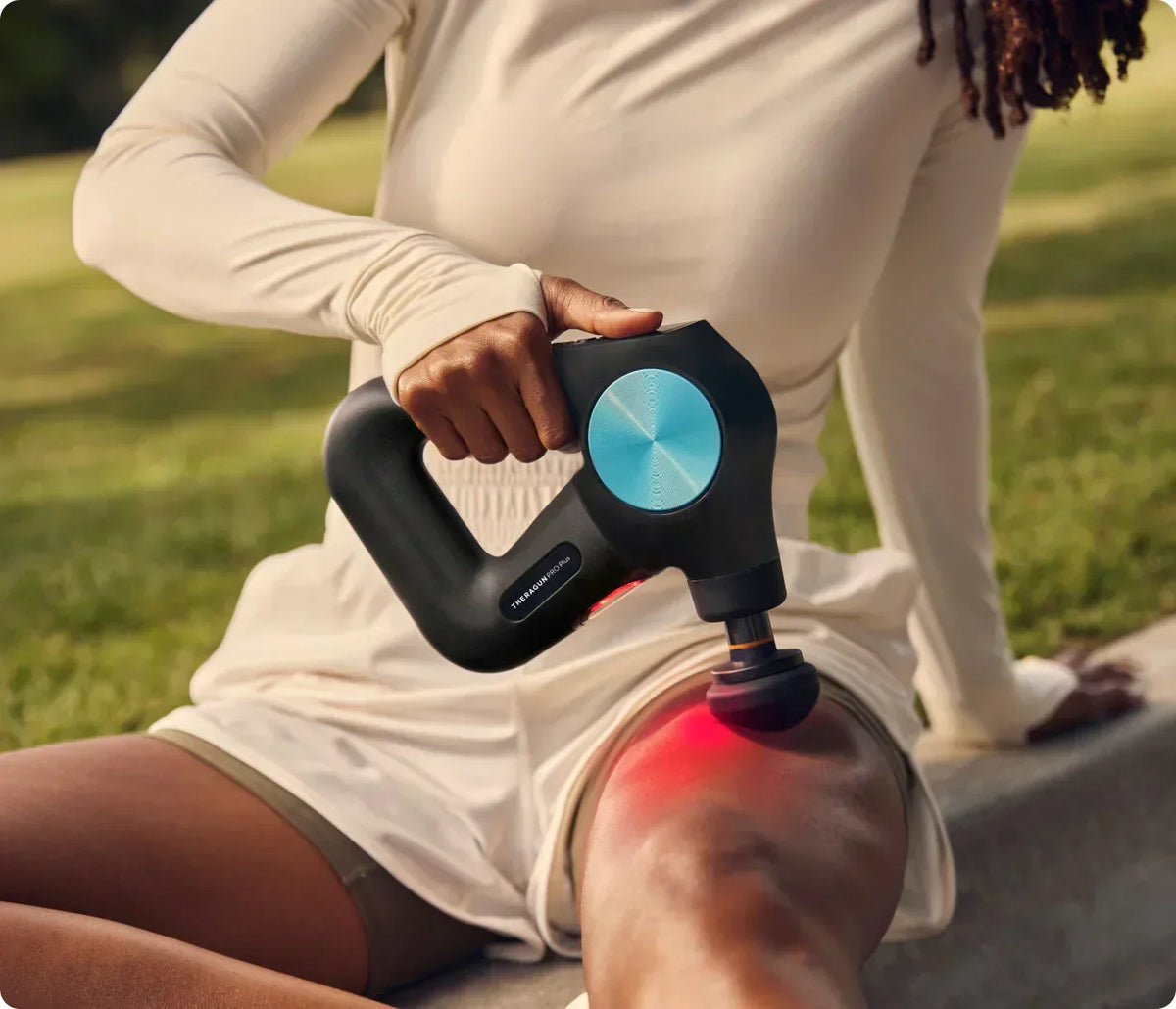 A person using a black Theragun massage gun with red light therapy on their thigh.