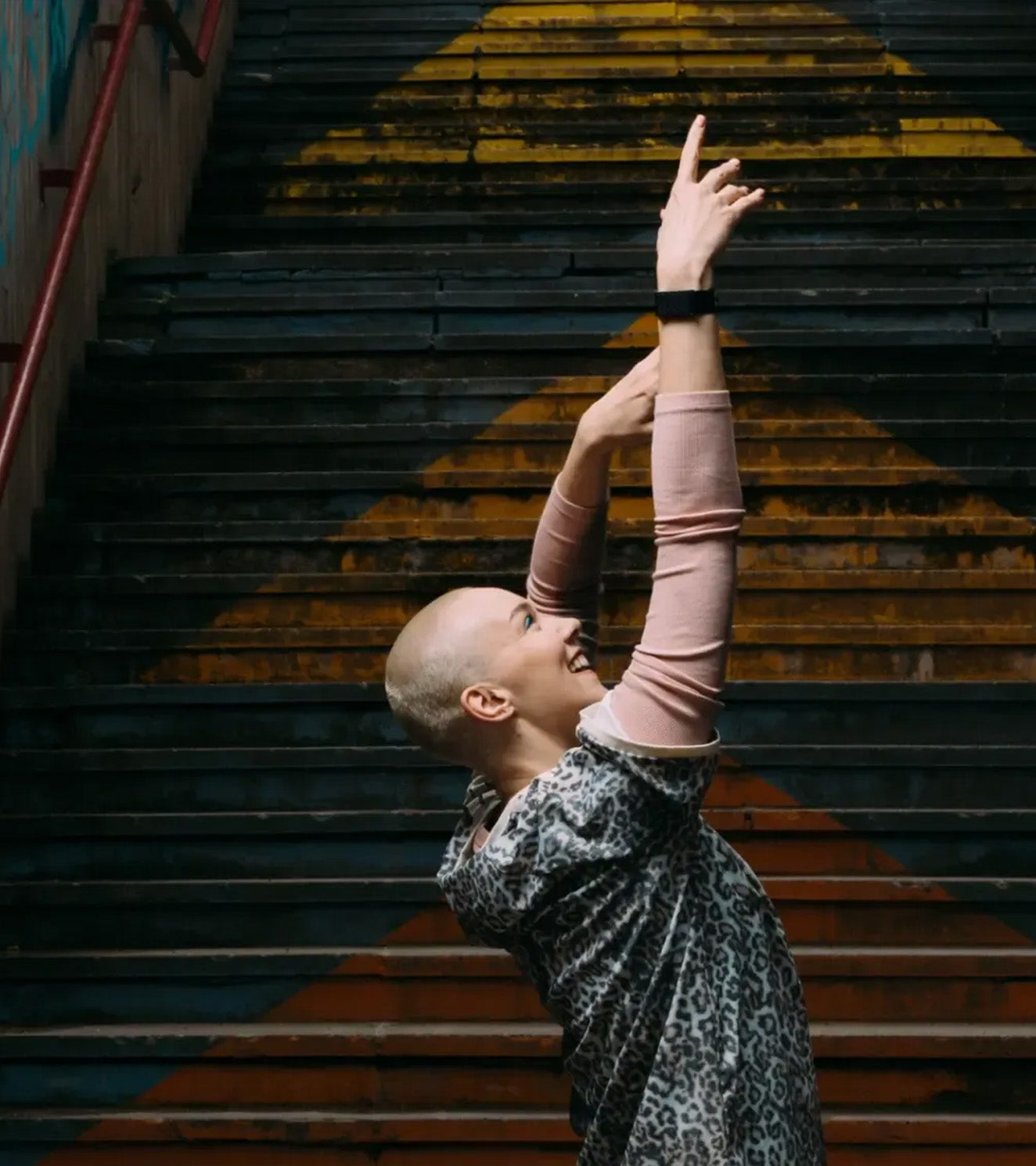 Smiling person stretching arms upward on painted urban stairs, fitness and wellness pose