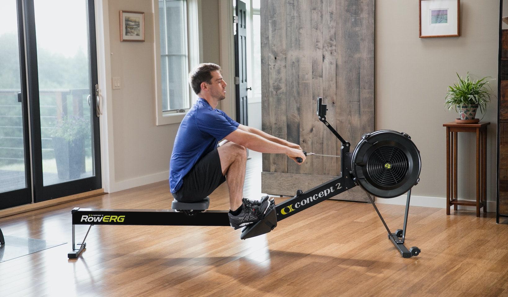 Man using Concept2 indoor rowing machine for functional fitness workout in a home gym