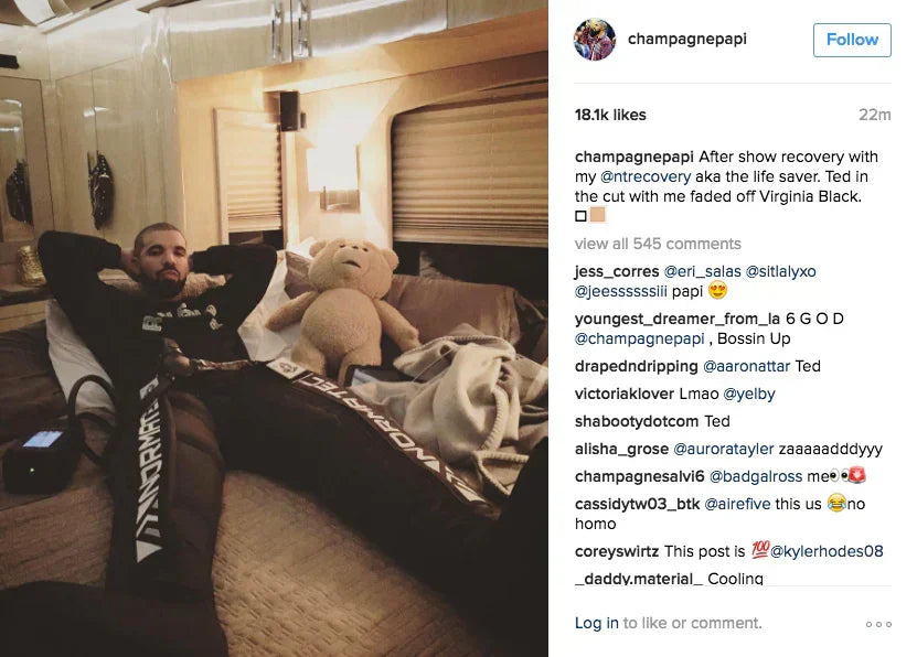 Drake relaxing in a lounge area wearing black athletic joggers and a black top.