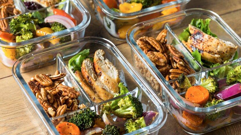 Meal prep containers with grilled chicken, pecans, broccoli, carrots, and fresh vegetables