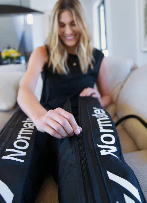 Woman using Normatec recovery compression leg sleeves on sofa for fitness recovery