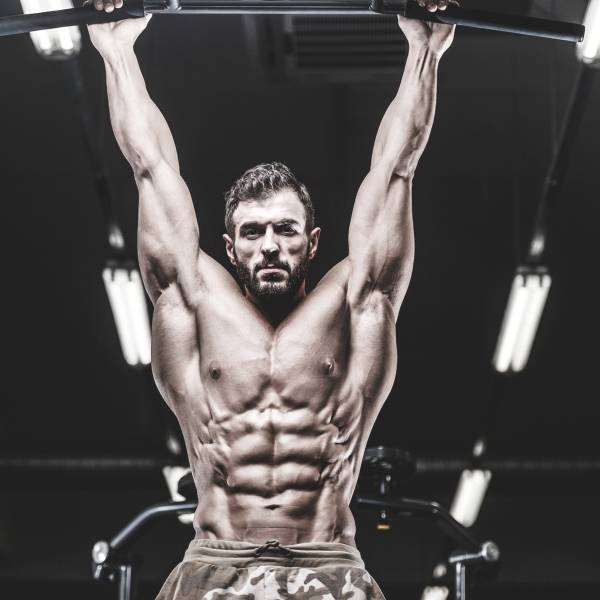 Muscular man performing pull-ups in gym, showcasing functional fitness and athletic strength