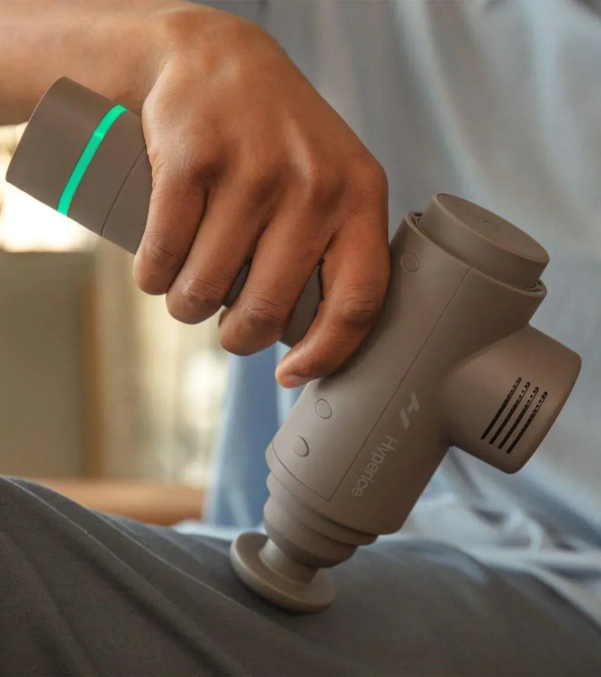 Person using a Hyperice percussion massage gun on their leg for muscle recovery.