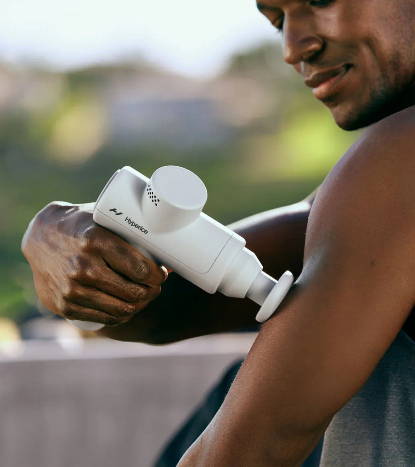 Man using white Hypervolt massage gun on upper arm outdoors