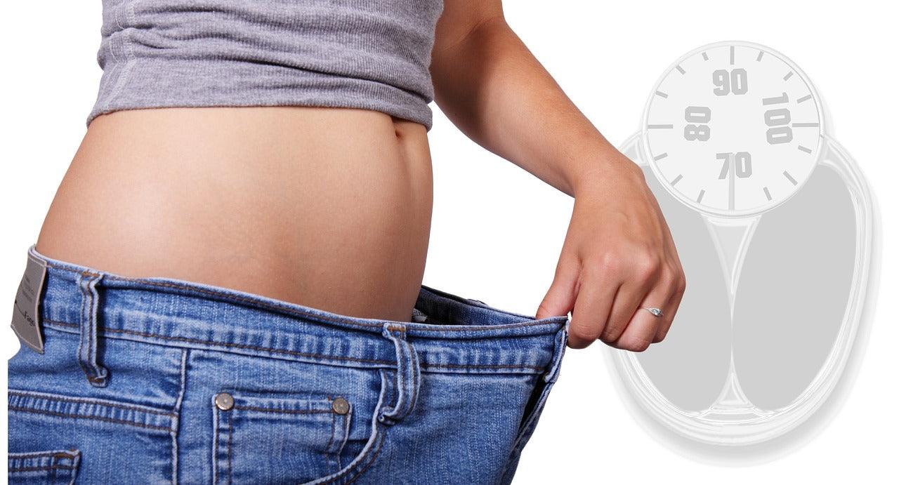 Person showing weight loss by wearing loose jeans, with a scale in the background