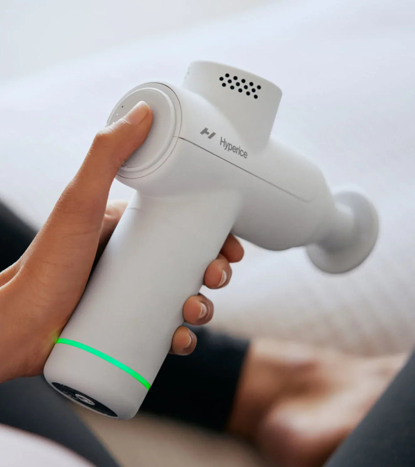 Hand holding a white Hyperice Hypervolt Go 2 portable massage gun with green LED light.