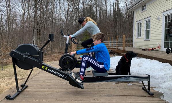 Boy using Concept2 rowing machine outdoors, woman cycling, winter fitness scene