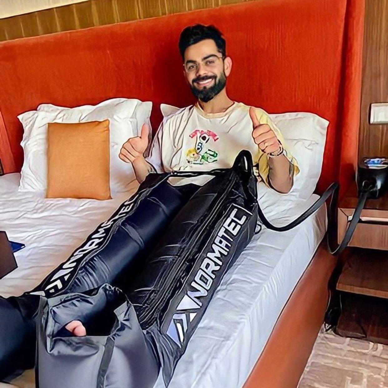Man using Normatec compression therapy boots for athletic recovery on a bed