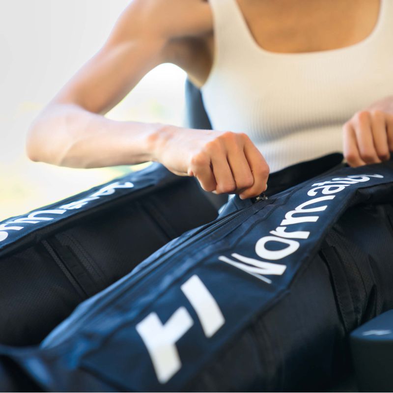 A person adjusting a Normatec compression leg sleeve for athletic recovery.