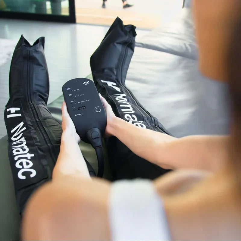 Athlete using Normatec leg recovery compression sleeves with control device indoors