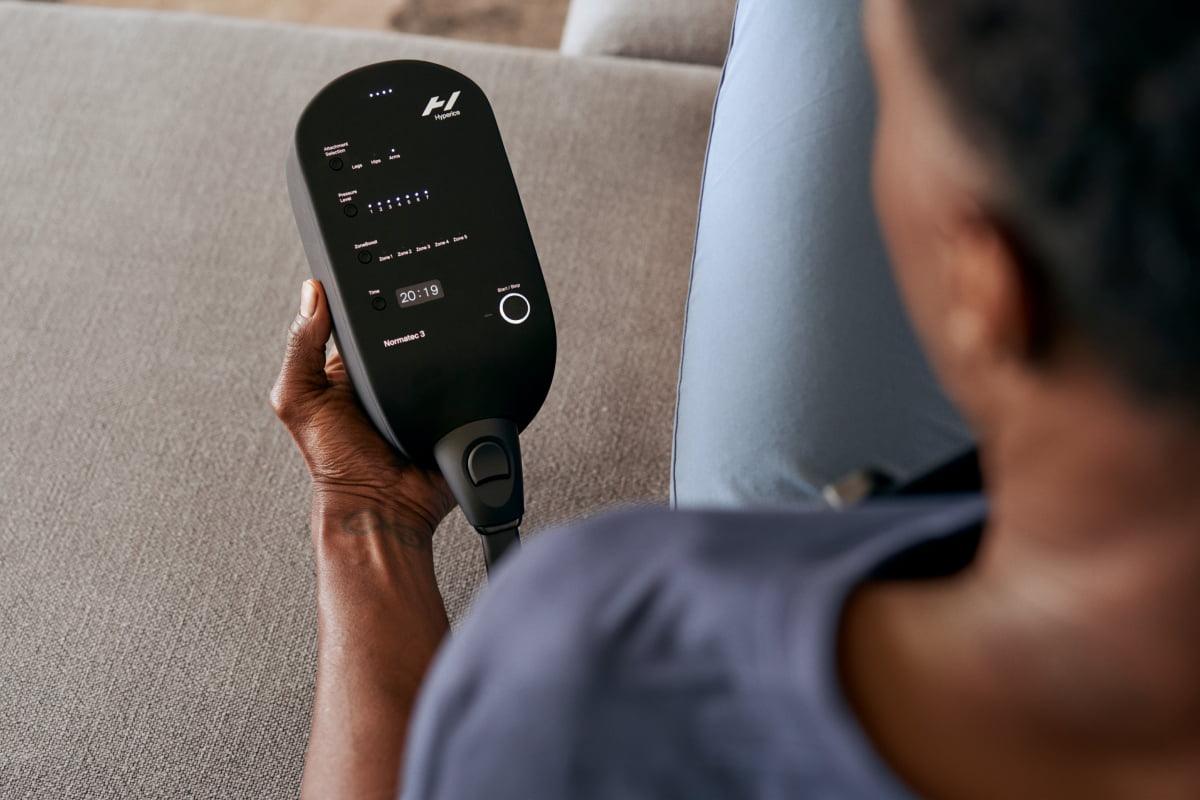 Person using a Normatec 3 recovery compression therapy device on a sofa