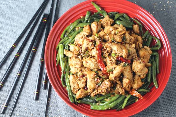 Sichuan chicken stir fry with fried green beans and red chili peppers on a red plate