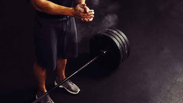Athlete preparing to lift loaded barbell in gym, chalking hands for functional fitness