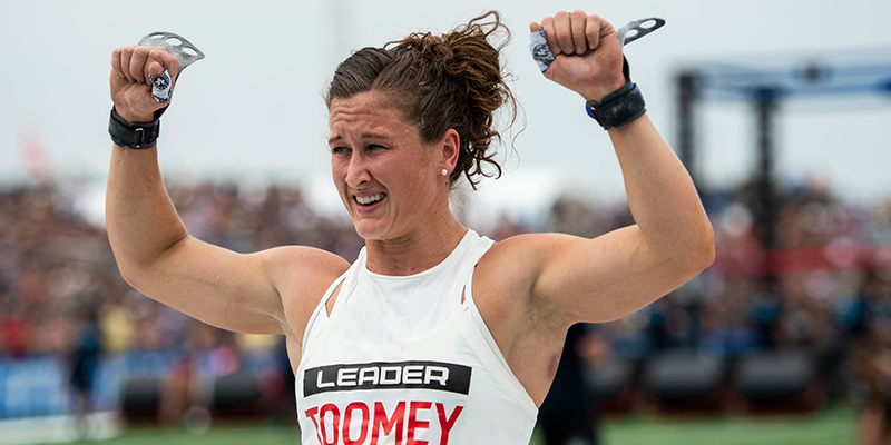 Female athlete in competition gear raising grip aids, fitness event crowd in background