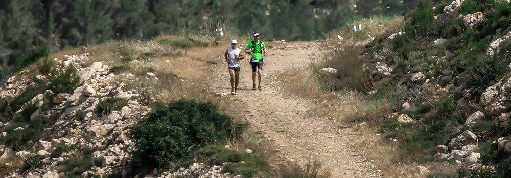 Two runners in athletic gear on a rocky trail, outdoors, long-distance running form