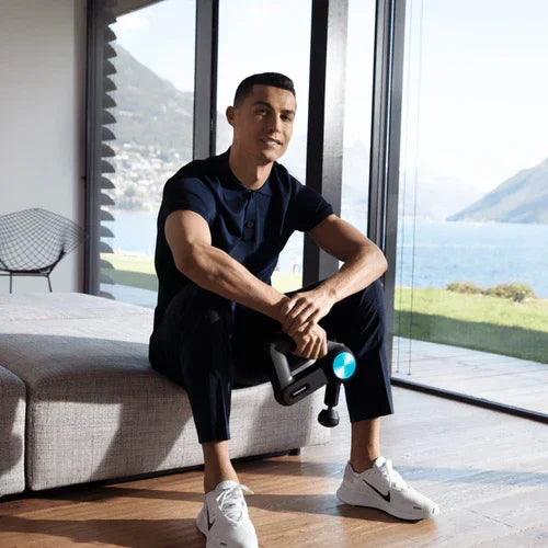 Man in sportswear using massage gun in modern living room with lake view