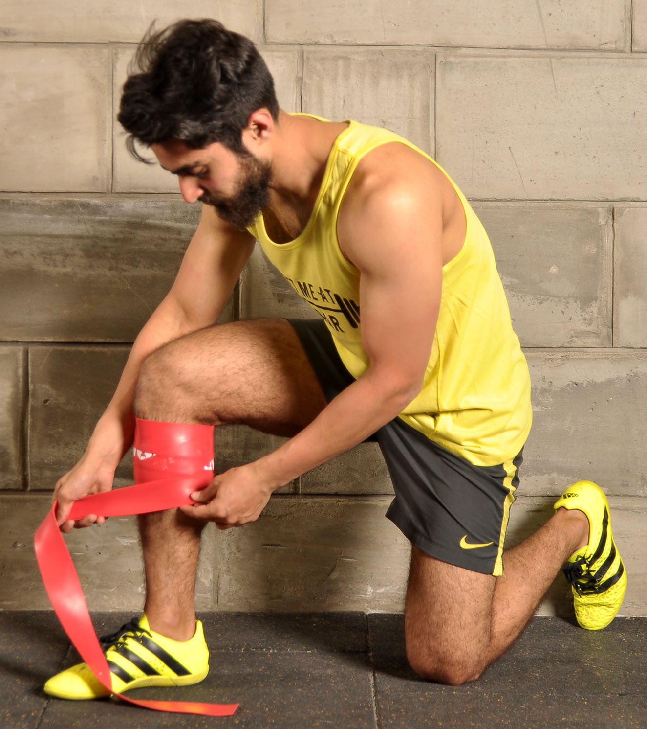 Athlete in yellow sportswear wrapping red resistance band around knee for functional fitness