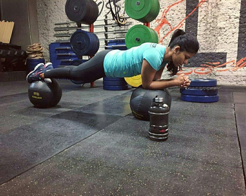 Woman doing plank exercise on medicine balls in a gym with weights and fitness equipment