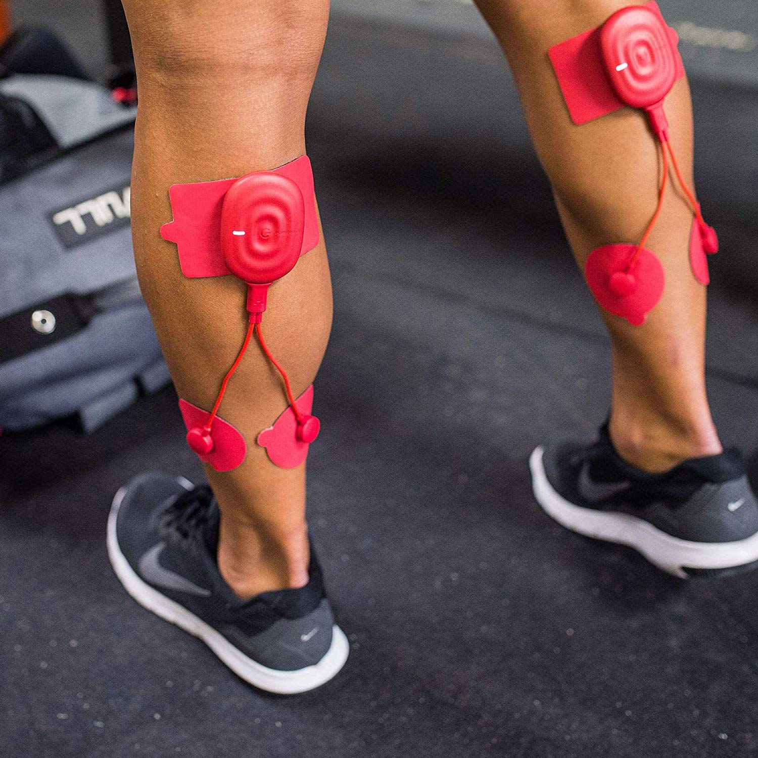 Athlete using red electrical muscle stimulation pads on calves in fitness gym setting