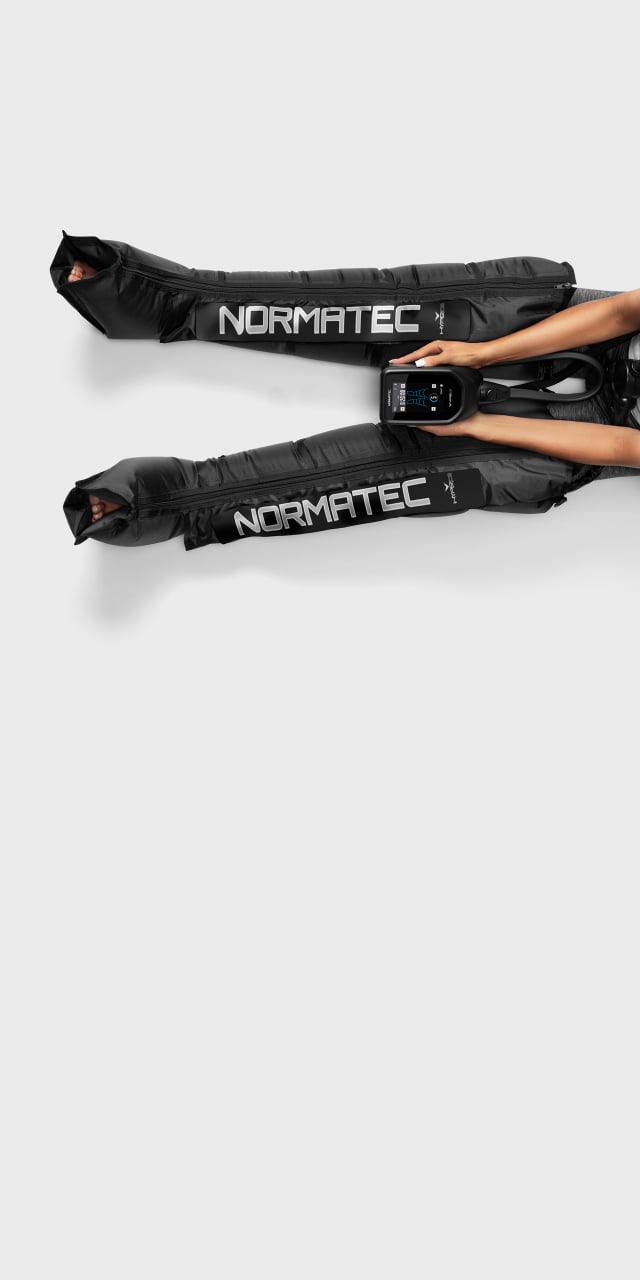 Person using Normatec 2.0 leg compression recovery sleeves on white background