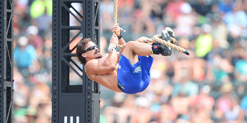 Male athlete in sunglasses climbing a rope during an outdoor functional fitness competition