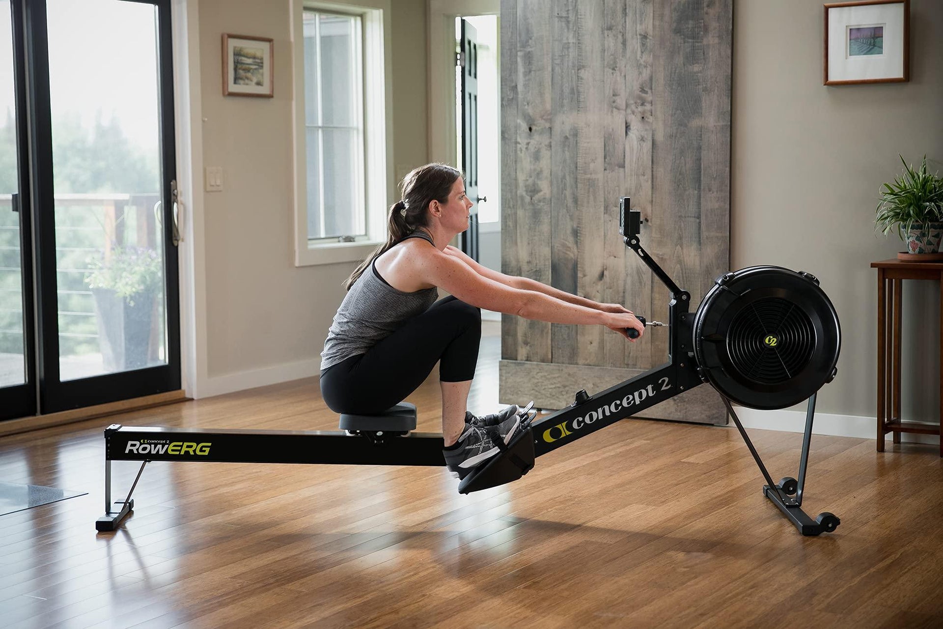 Woman using a Concept 2 rowing machine indoors on wooden floor for full body workout