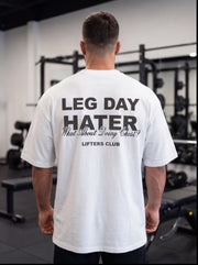Man wearing white 'Leg Day Hater' gym t-shirt in fitness studio, perfect for lifters and workout humor.