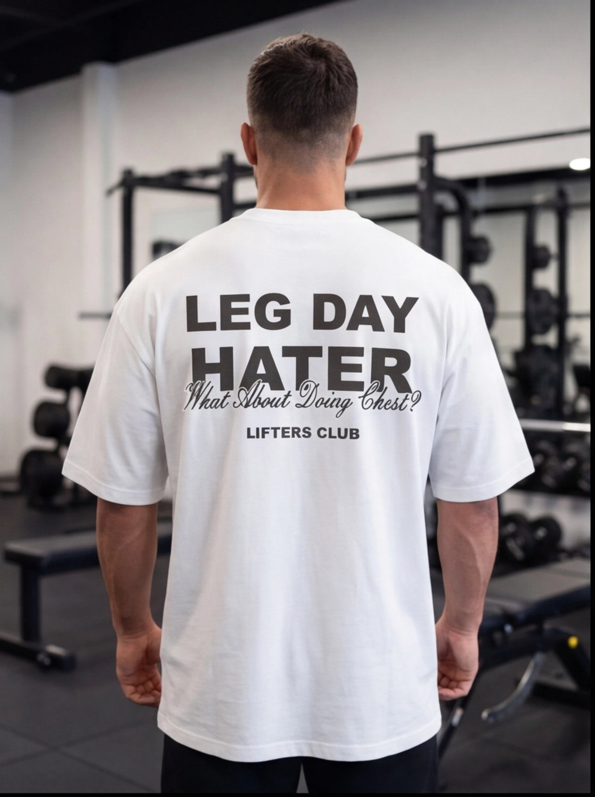 Man wearing white 'Leg Day Hater' gym t-shirt in fitness studio, perfect for lifters and workout humor.