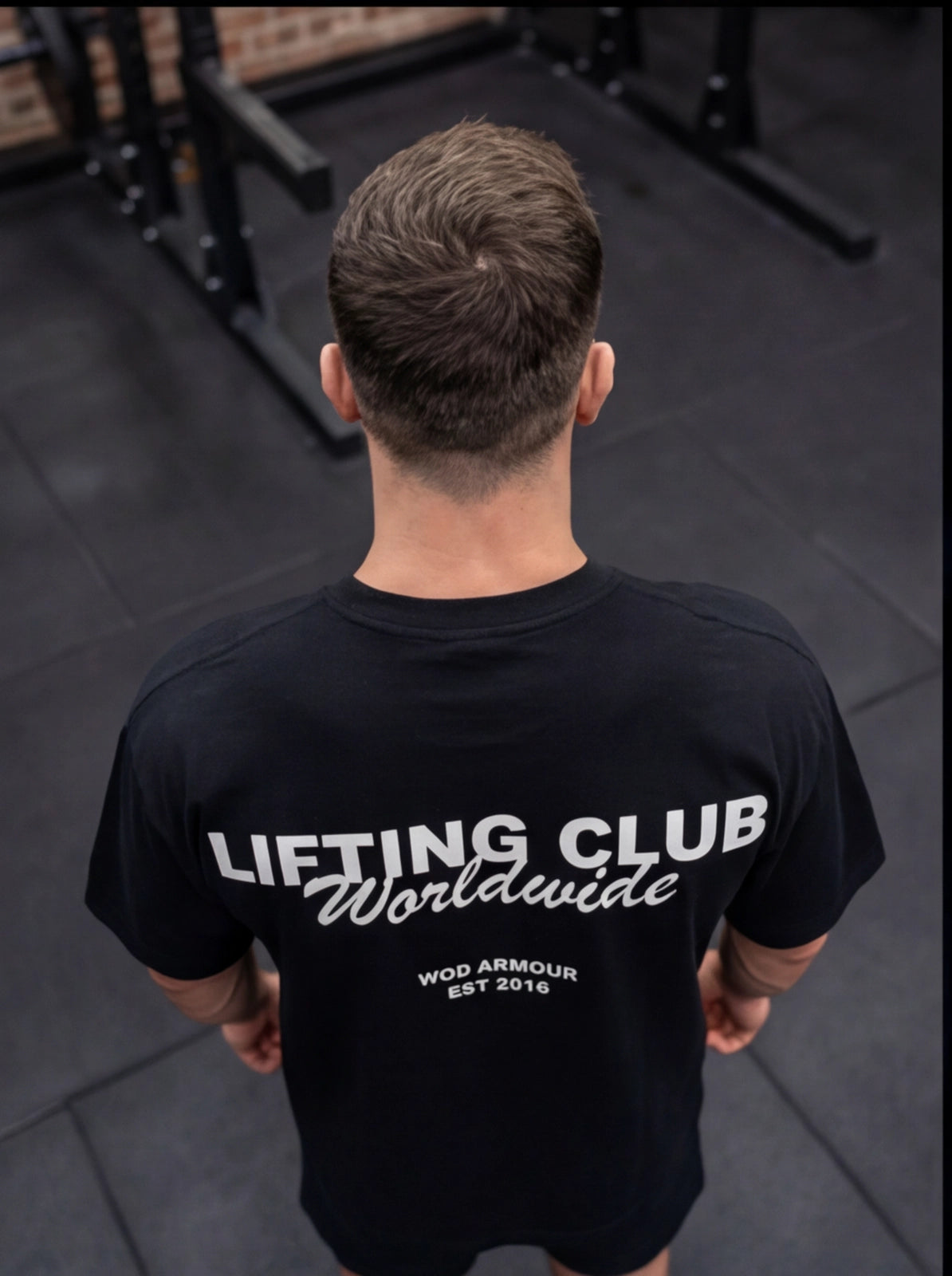 Man wearing black 'Lifting Club Worldwide' gym t-shirt, back view in fitness studio