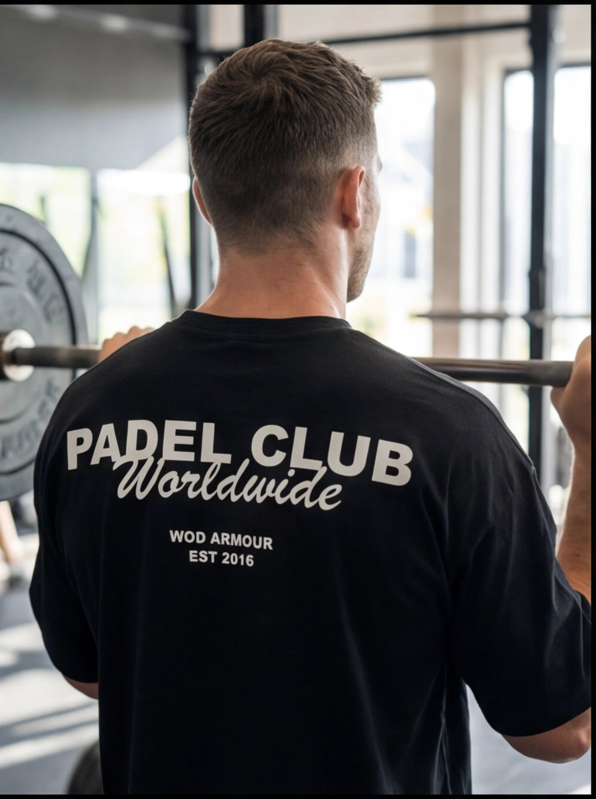 Man lifting barbell in gym wearing black Padel Club Worldwide WOD Armour t-shirt, functional fitness apparel