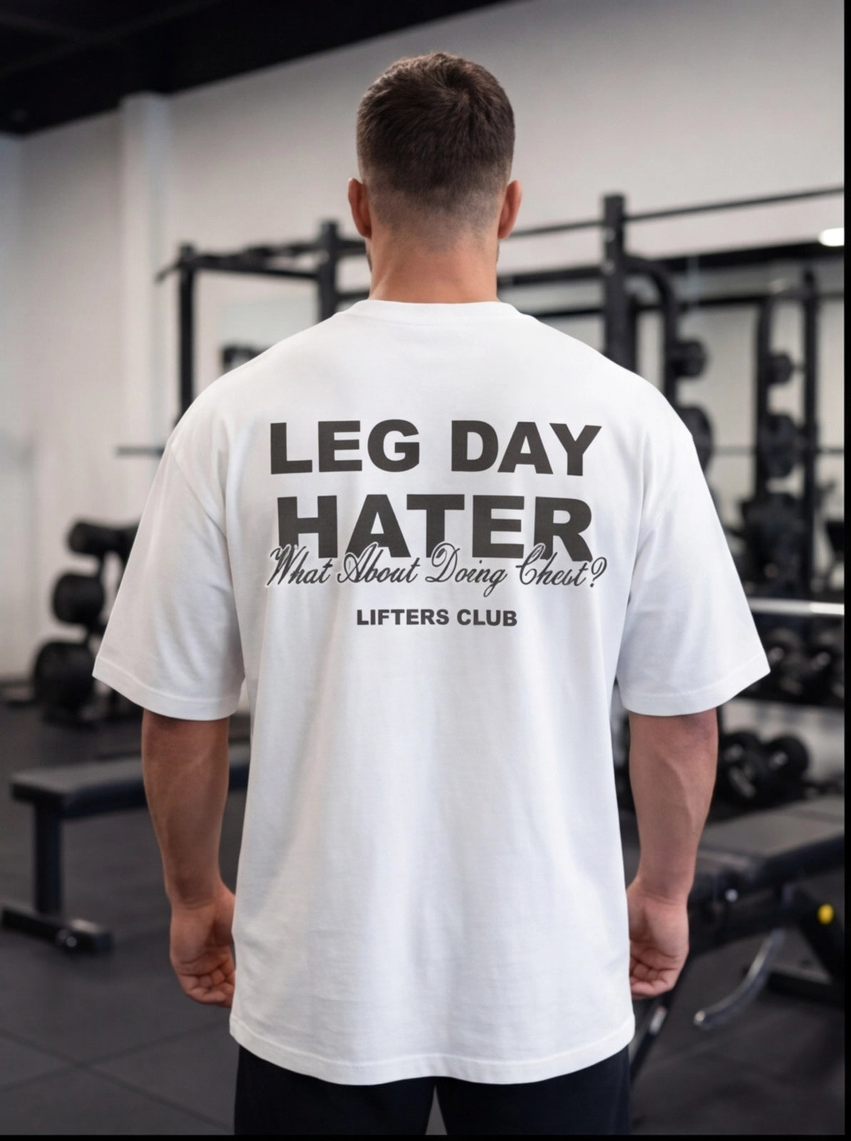 Man wearing white 'Leg Day Hater' gym t-shirt in fitness studio, lifting gear background