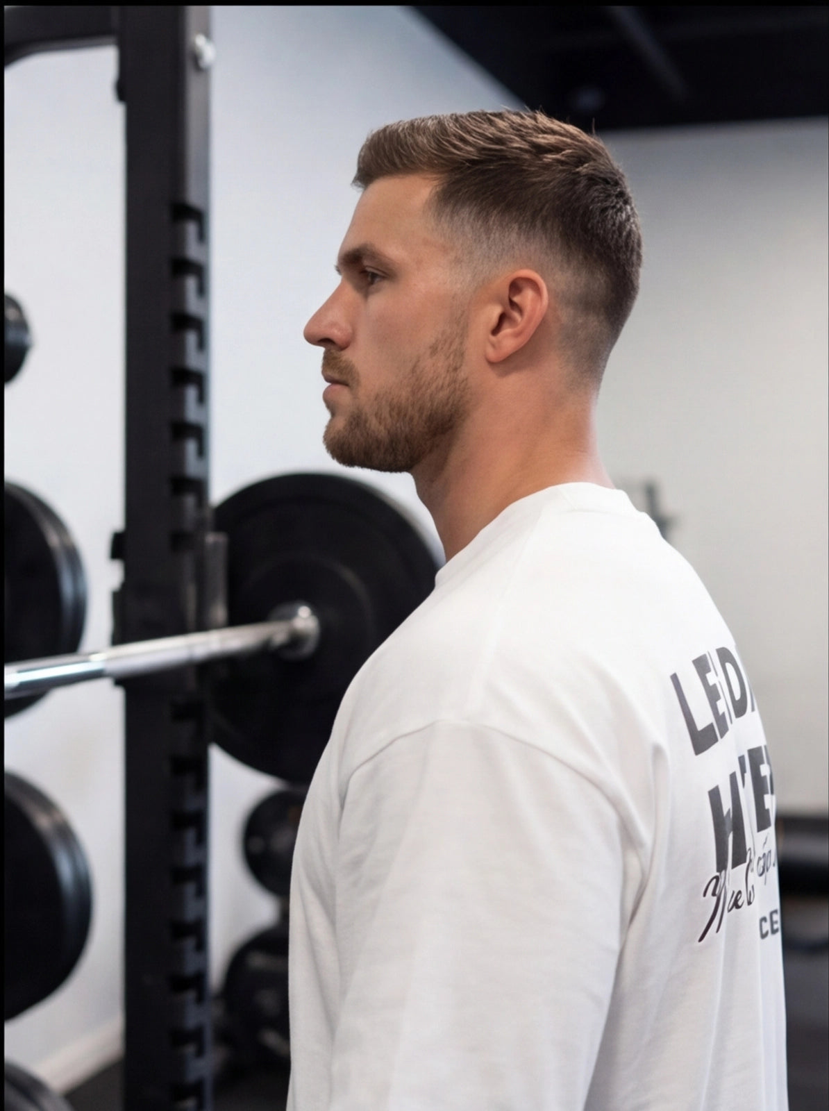 Man in white gym shirt at weight rack, functional fitness apparel for athletes