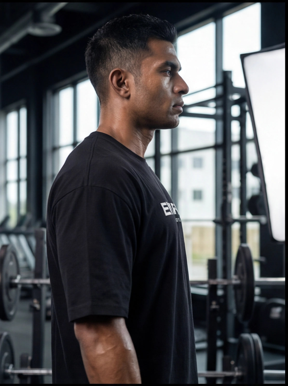 Athlete in black gym t-shirt at functional fitness facility with weight racks and barbells