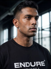 Athlete in black ENDURE t-shirt, focused expression in gym setting for functional fitness training.