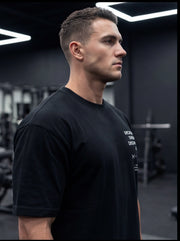 Athlete in black gym t-shirt with white text, standing in modern fitness studio