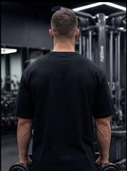 Man in black gym shirt holding dumbbells, back view in fitness center