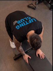 Man in black 'Lifting Club' shirt performing gym exercise on bench, showcasing functional fitness apparel.